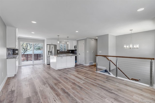 kitchen featuring light wood-type flooring, backsplash, an inviting chandelier, and white cabinets