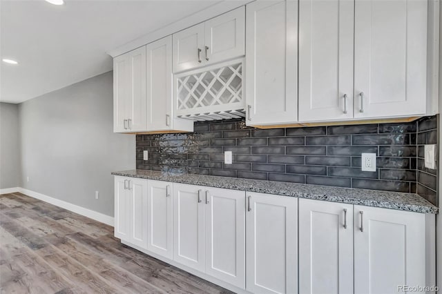 kitchen with light wood-style flooring, tasteful backsplash, white cabinetry, stone counters, and baseboards