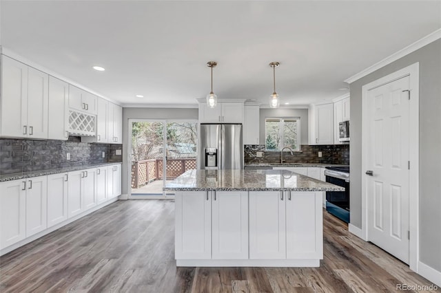 kitchen with a sink, wood finished floors, appliances with stainless steel finishes, white cabinets, and crown molding