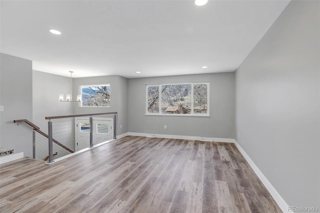 empty room with a chandelier, recessed lighting, baseboards, and wood finished floors