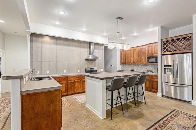 kitchen featuring stainless steel appliances, a sink, a kitchen island, wall chimney exhaust hood, and pendant lighting