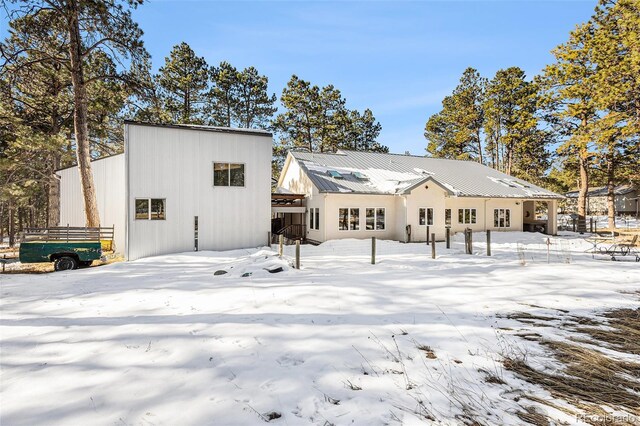 snow covered back of property featuring metal roof and fence