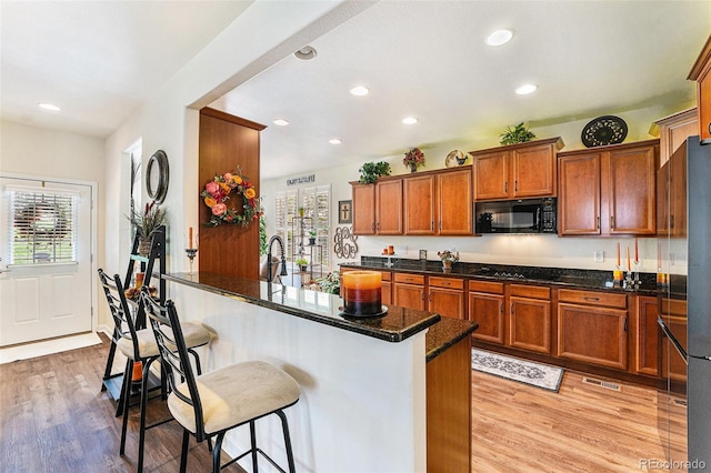19780 W 57th Ln, Golden, CO 80403 - kitchen with black microwave, a kitchen breakfast bar, brown cabinetry, light wood-style floors, and recessed lighting