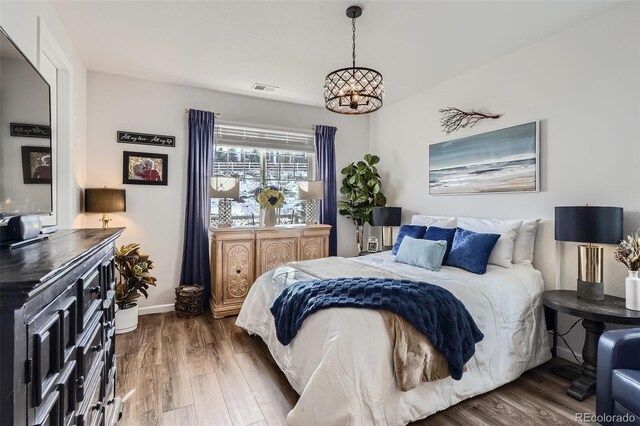 bedroom featuring baseboards, visible vents, wood finished floors, and an inviting chandelier