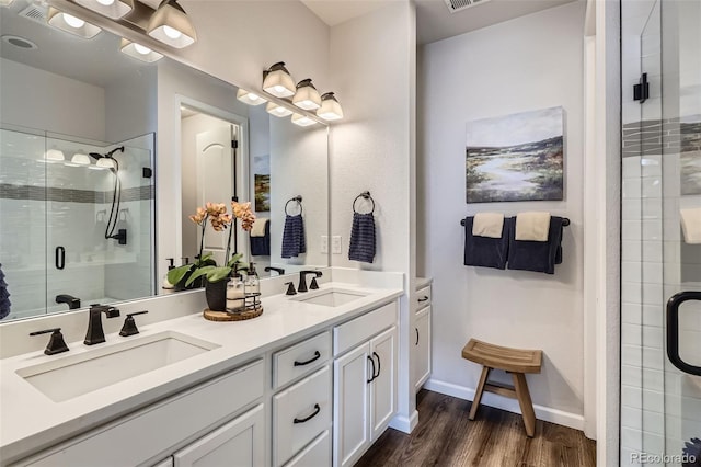 full bath with a sink, a stall shower, double vanity, and wood finished floors