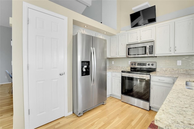 kitchen with high vaulted ceiling, white cabinets, stainless steel appliances, and light hardwood / wood-style floors