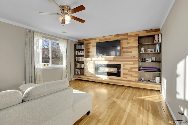 living room featuring hardwood / wood-style floors, ceiling fan, crown molding, and wooden walls