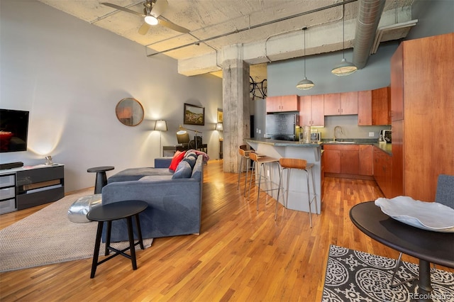 living room featuring a towering ceiling, light hardwood / wood-style floors, ceiling fan, and sink