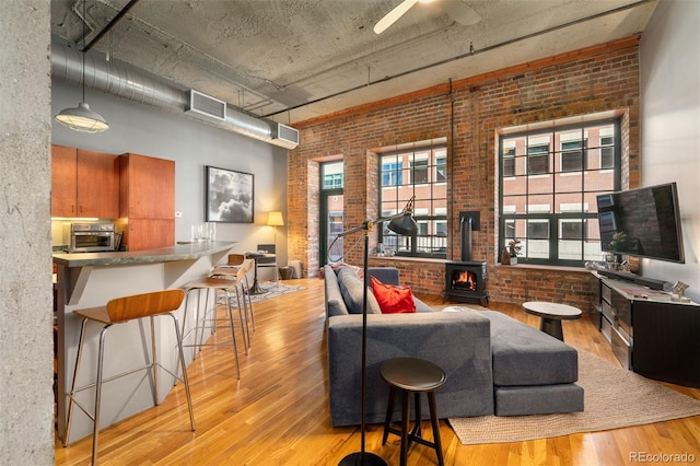 living room with light hardwood / wood-style flooring, a wood stove, ceiling fan, and brick wall