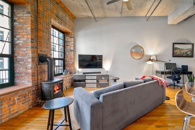 living room with a wood stove, ceiling fan, brick wall, and light wood-type flooring