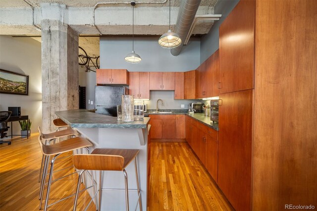 kitchen featuring sink, hanging light fixtures, light hardwood / wood-style flooring, a towering ceiling, and a breakfast bar area