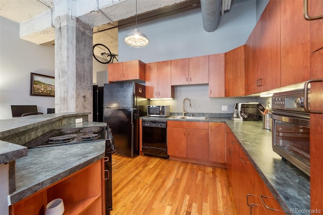 kitchen featuring sink, a towering ceiling, pendant lighting, light hardwood / wood-style floors, and black appliances