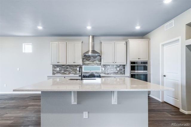 4947 N Quatar St, Aurora, CO 80019 - kitchen with wall chimney exhaust hood, double oven, tasteful backsplash, an island with sink, and a breakfast bar area