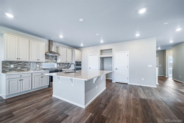 4947 N Quatar St, Aurora, CO 80019 - kitchen featuring stainless steel appliances, wall chimney range hood, light countertops, tasteful backsplash, and dark wood-type flooring