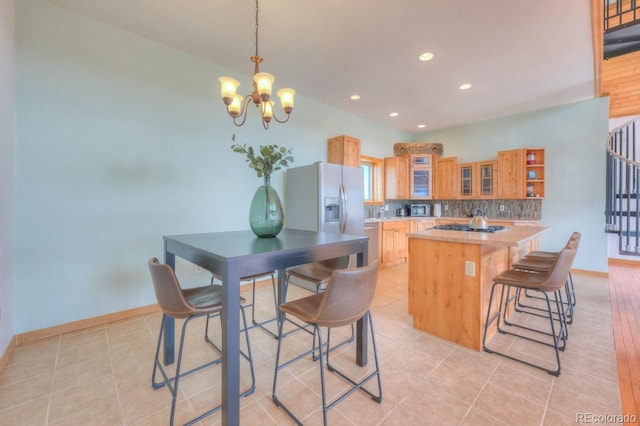 kitchen with appliances with stainless steel finishes, tasteful backsplash, an inviting chandelier, an island with sink, and light tile patterned flooring