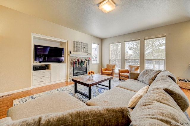 living room featuring a textured ceiling, light wood-type flooring, and a tiled fireplace