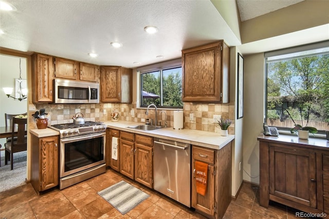 kitchen featuring stainless steel appliances, a sink, plenty of natural light, brown cabinetry, and a textured ceiling