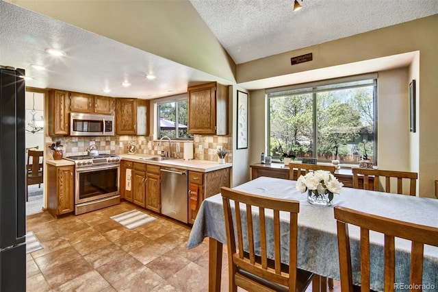 kitchen with stainless steel appliances, a textured ceiling, a sink, backsplash, and brown cabinets