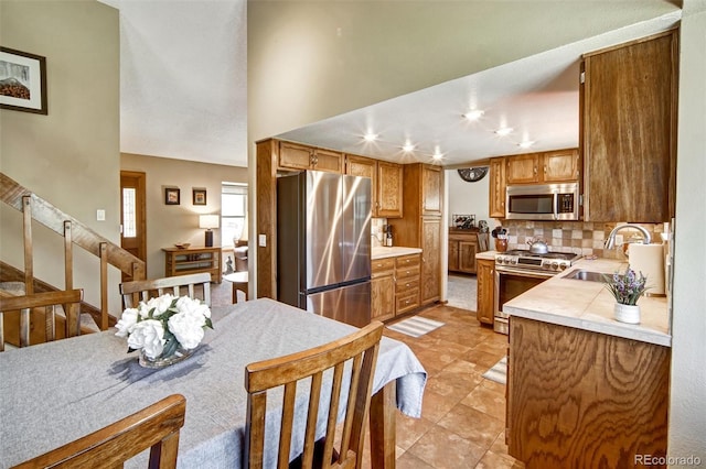 kitchen featuring stainless steel appliances, a sink, light countertops, decorative backsplash, and brown cabinets
