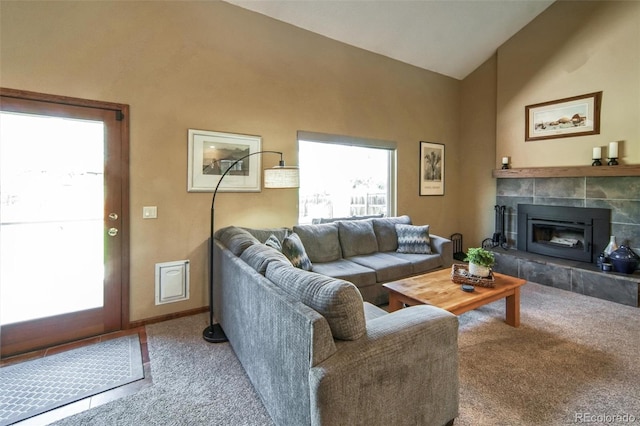living area featuring vaulted ceiling, carpet, healthy amount of natural light, a tiled fireplace, and baseboards
