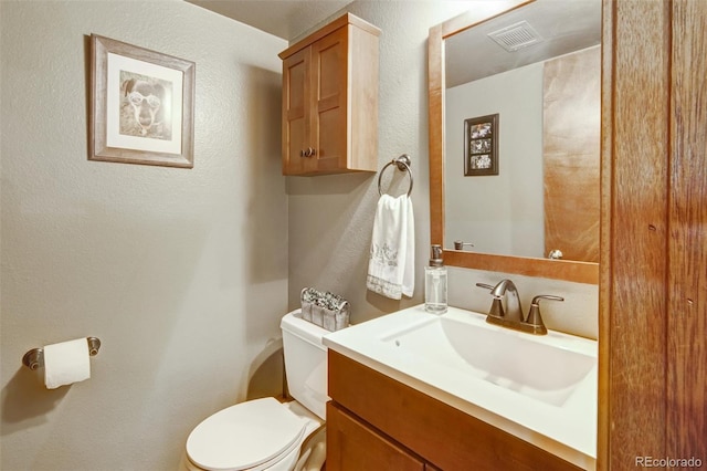 bathroom featuring toilet, vanity, and a textured wall