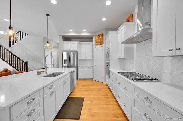 6632 Osage St, Denver, CO 80221 - kitchen with wall chimney range hood, a sink, stainless steel appliances, light wood-style floors, and white cabinets