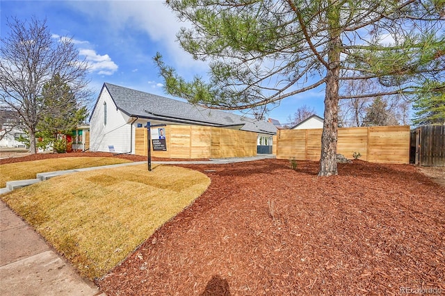 exterior space featuring roof mounted solar panels, roof with shingles, and fence