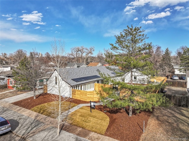 view of front of property featuring concrete driveway, fence, and roof mounted solar panels