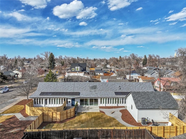 back of property featuring a residential view, roof with shingles, a fenced backyard, and a sunroom
