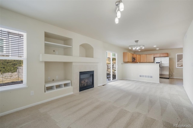 unfurnished living room featuring built in features, light colored carpet, visible vents, a tiled fireplace, and baseboards