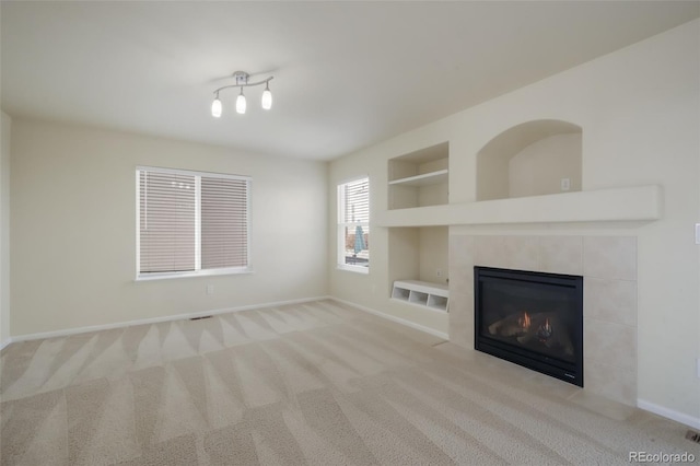 unfurnished living room featuring built in features, a tile fireplace, carpet flooring, and baseboards