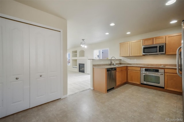 kitchen with recessed lighting, appliances with stainless steel finishes, a glass covered fireplace, a sink, and a peninsula