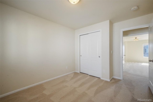 unfurnished bedroom featuring light carpet, a closet, and baseboards