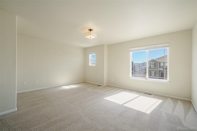 carpeted spare room featuring plenty of natural light, visible vents, and baseboards