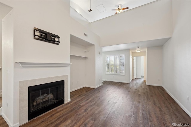 unfurnished living room with visible vents, baseboards, a tile fireplace, dark wood-style floors, and ceiling fan