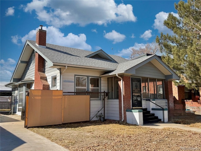 view of front of home featuring brick siding, roof with shingles, a chimney, and fence