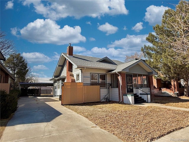 view of front facade with a chimney, fence, concrete driveway, a carport, and brick siding