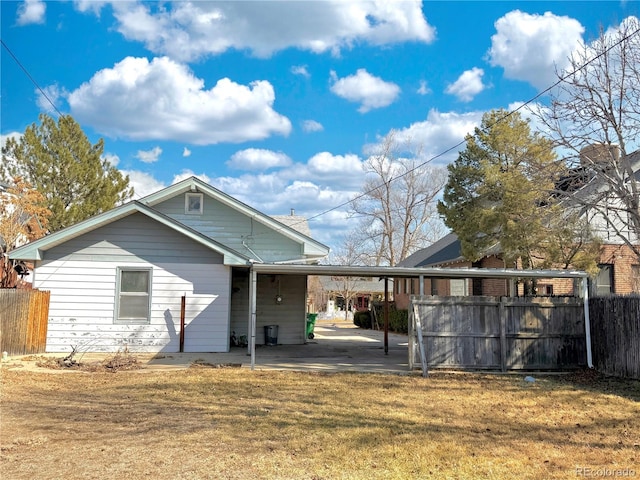 rear view of house featuring a carport, a lawn, and fence