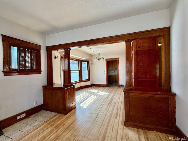 unfurnished room featuring a notable chandelier, light wood-style flooring, baseboards, and decorative columns