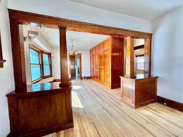 interior space featuring a chandelier, baseboards, light wood-style flooring, and ornate columns