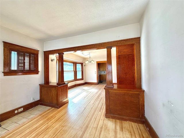 unfurnished room with a notable chandelier, a textured ceiling, light wood-style floors, and decorative columns