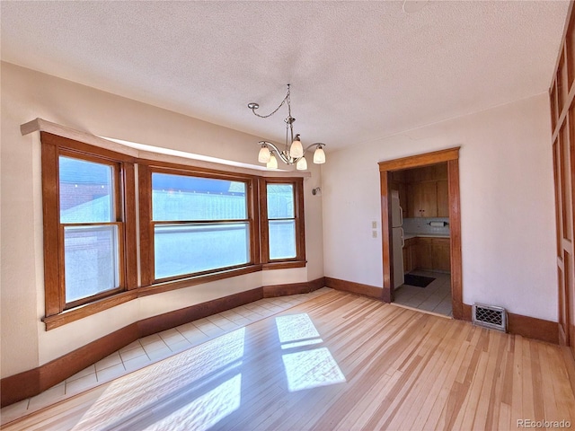 unfurnished dining area featuring visible vents, light wood-style flooring, a textured ceiling, and an inviting chandelier