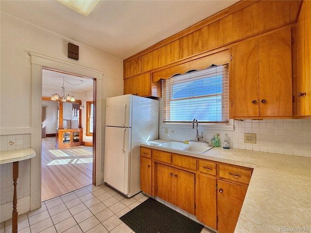 kitchen featuring light tile patterned floors, freestanding refrigerator, a sink, light countertops, and tasteful backsplash