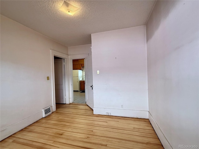 unfurnished room with visible vents, a textured ceiling, light wood-type flooring, and baseboards