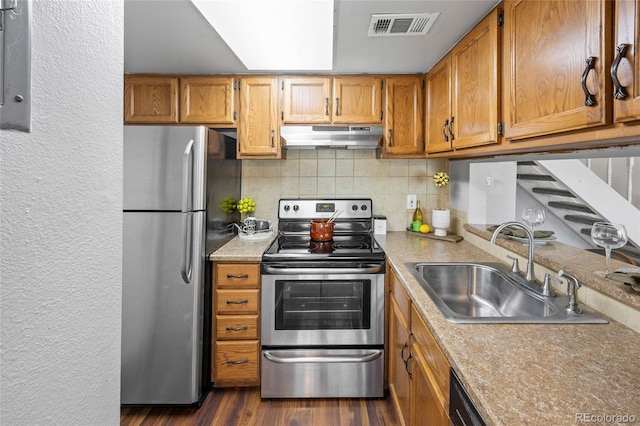 1250 S Monaco Pkwy Unit 50, Denver, CO 80224 - kitchen with stainless steel appliances, under cabinet range hood, decorative backsplash, brown cabinets, and a textured wall