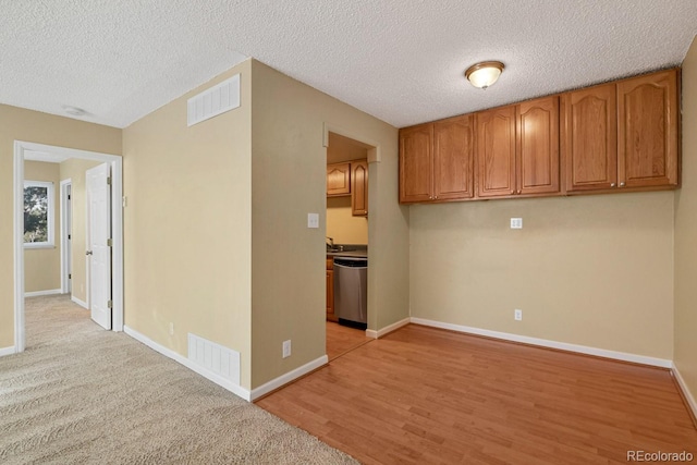1195 S Oneida St Unit E, Denver, CO 80224 - kitchen with brown cabinets, stainless steel dishwasher, a textured ceiling, and light wood-style flooring