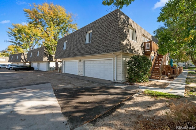 1195 S Oneida St Unit E, Denver, CO 80224 - view of property exterior featuring a shingled roof, driveway, mansard roof, an attached garage, and stairs
