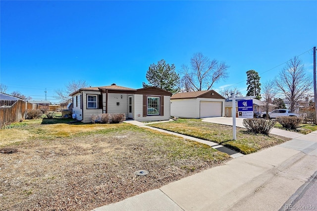 view of front facade with a detached garage, fence, concrete driveway, a front yard, and an outdoor structure