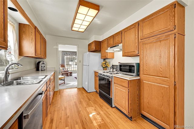 kitchen with light wood finished floors, a sink, stainless steel appliances, light countertops, and under cabinet range hood