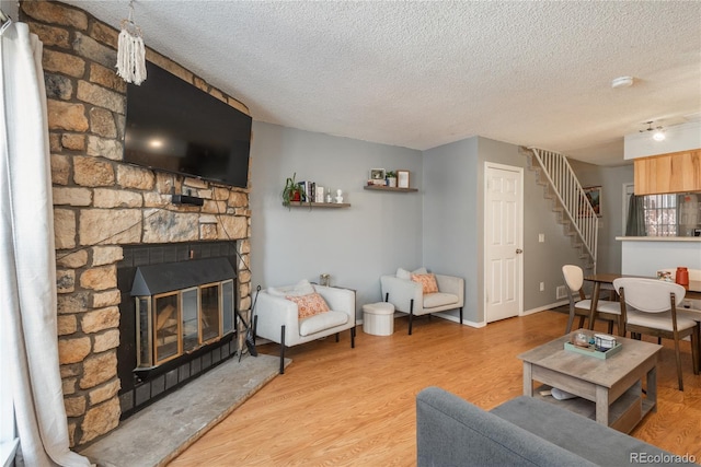 living area featuring a textured ceiling, wood finished floors, stairway, a stone fireplace, and baseboards